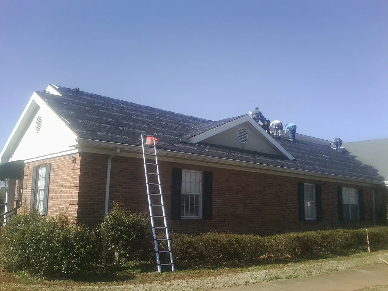 Crew tearing shingles off a brick ranch roof with a ladder set — Emergency Roof Repair work by our crew in Goodhue