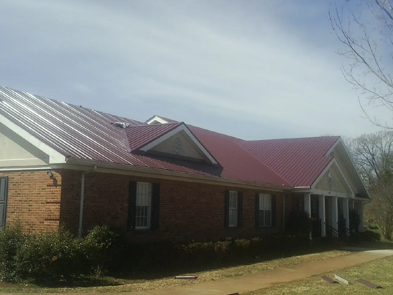 Red metal roof with gabled entries on a long brick building, from a Hail Damage Roof Repair job in Goodhue