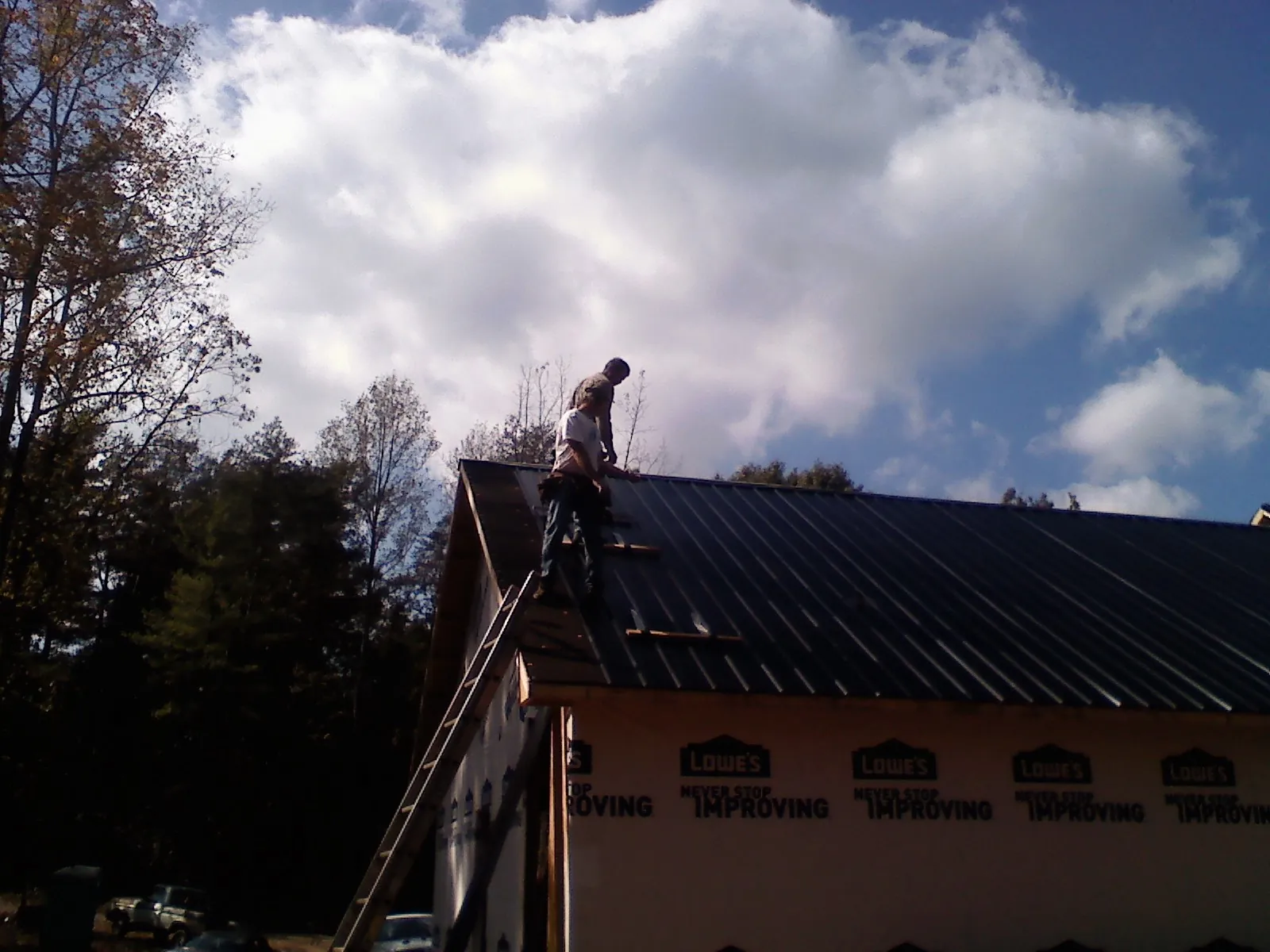 Roofer fastening dark metal panels high against a cloudy sky, from a Roof Inspection job in Goodhue