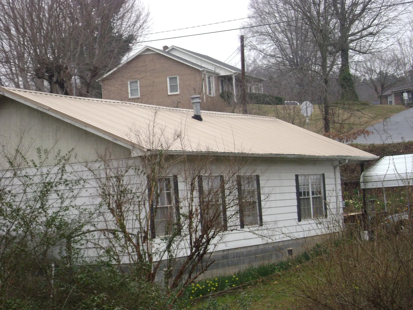 Tan metal roof on a white sided house set into a hillside — Commercial Roofing by Roofing Brothers in Goodhue