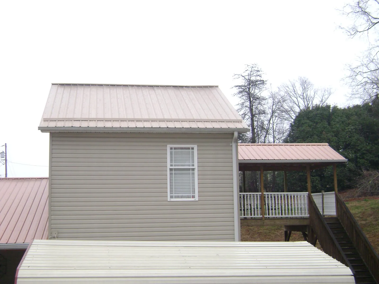 Tan metal roofs on a two story addition and attached porch, from a Roof Replacement job in Goodhue